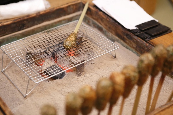 ↑いま雪江さんが囲炉裏で焼く名物のいしりもち(1本300円)。イカのはらわたを使った魚醤(魚を原料とする醤油)、「いしる」で炊いたもち米と飯米を半つぶしにして、青のりやゴマで味を整え、竹の棒に巻きつけて炙ったもの。関西火鉢に炭が入る冬場のみ味わえ