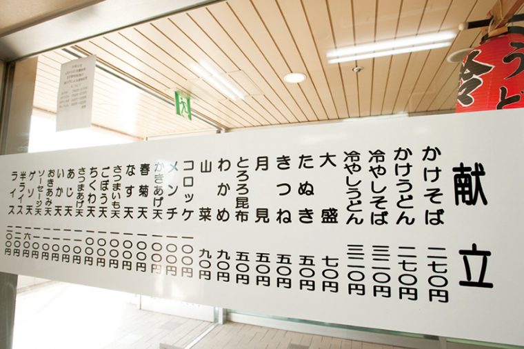 ↑店頭の窓ガラスに貼られたメニュー表。多彩なトッピングは「かけそば」などの基本の麺と組み合わせて注文する