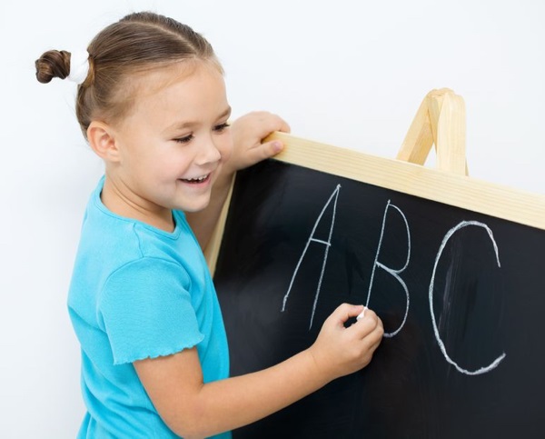 16336115 - cute little girl is writing letters on a blackboard in school