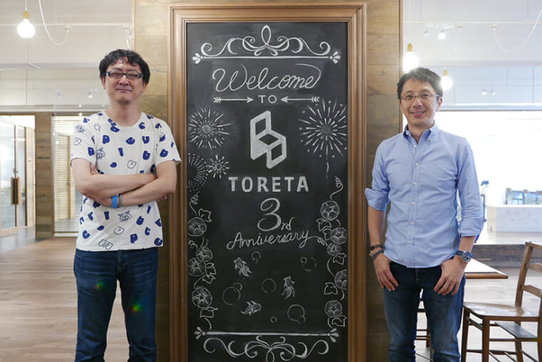 ↑サービス開始から3年目であることを知らせるブラックボードをはさんで。代表取締役 中村仁氏(右)と取締役COO 吉田健吾氏(左)