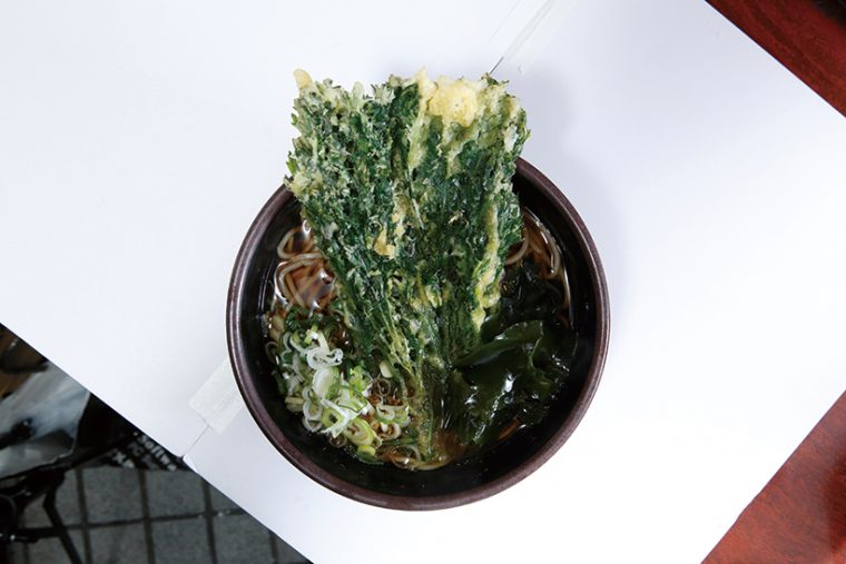 ↑春菊そば(430円)迫力満点な春菊天は、香り高く心地よい苦味がある。そばは適度なコシともっさり食感で、立ち食いそば 好きのツボにハマる。