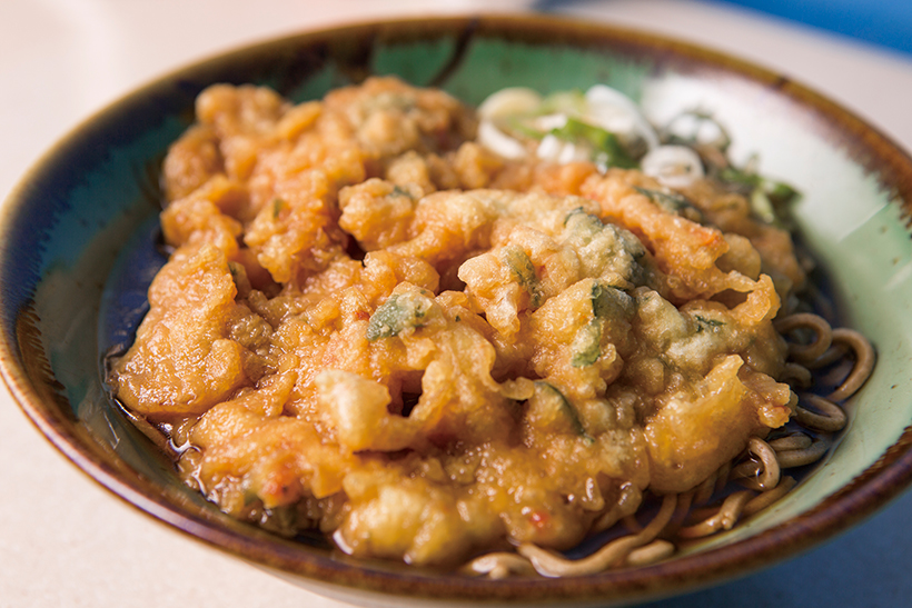 ↑天ぷらそば(350円)。かき揚げの中身は玉ねぎ、にんじ ん、春菊、干しエビ。衣が厚めだが、 この暗黒汁を吸うと、衣自体がごちそ うになる