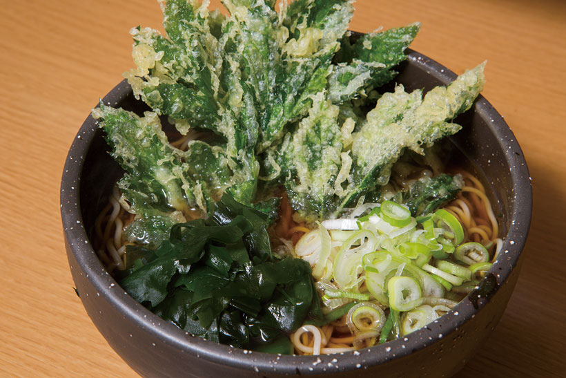 ↑明日葉天そば(380円)。どんぶりに寄りかかる大ぶりの明日葉 天が存在感あり。明日葉は独特の風味 で、あとからくるほろ苦さが魅力だ