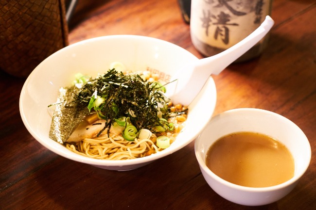 背あぶらーめん納豆(¥750)。ミニスープが添えられる、うれしいサービスも。ちなみに奥に見えるのは太久保酒造(鹿児島)の芋焼酎 杜の妖精¥550。アキラさん曰く「焼酎のラインナップは力入ってると思う!」とのこと。確かにプレミア酒の森伊蔵が¥650で置いてあるなど、侮れません!