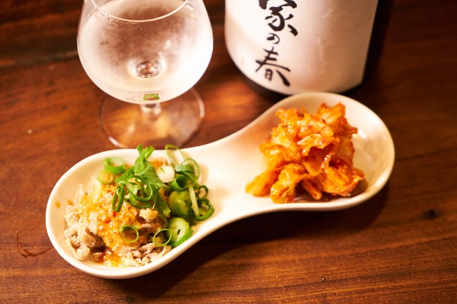 センマイ刺(¥580)。付け合わせの逸品が添えられるのも魅力で、こちらにはキムチが。日本酒はあづまみね(岩手)の純米吟醸 我が家の春(半合/¥480)。希少な銘柄も普通にそろっています。提供価格は銘柄問わず半合で¥480!