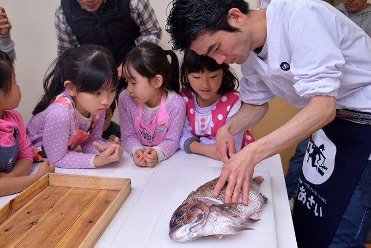 ↑鯛のおかしら付きの造りを完成させたのは浅井さん。子どもたちは興味津々