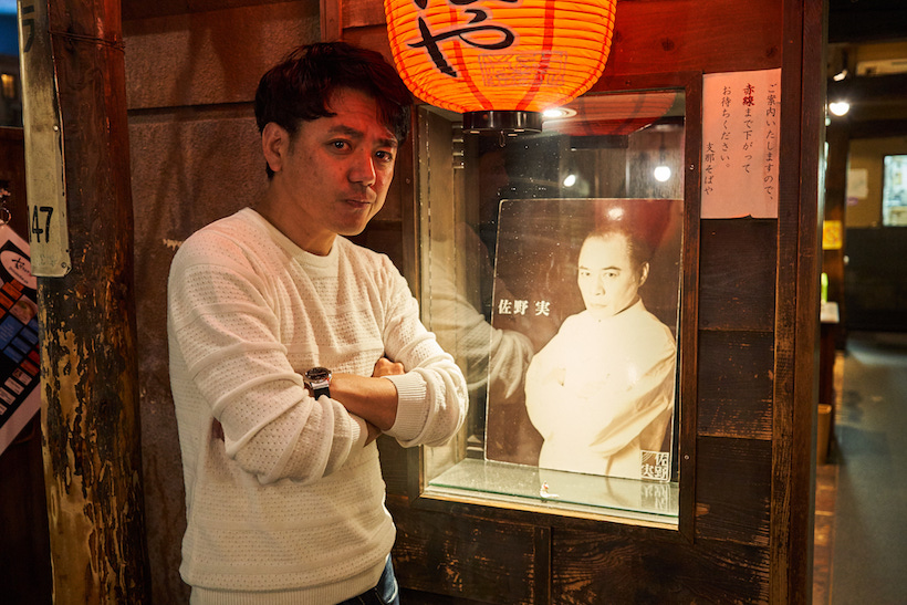 ↑入口の脇に飾られた佐野 実さんの写真と一緒に。田中さんももちろん生前のご本人に会ったことがあり、佐野さんを慕う多くのラーメン店主とも仲がいい