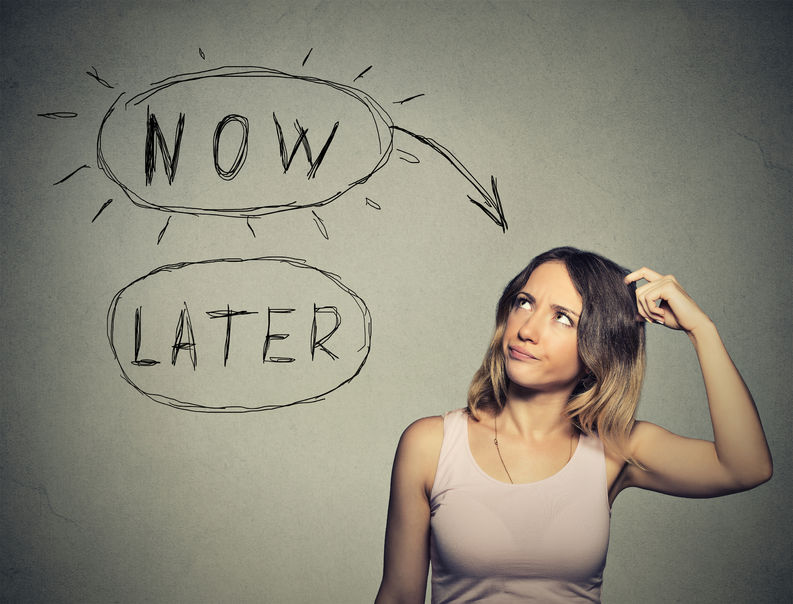 42814198 - now or later. woman thinking scratching head looking up isolated on grey wall background. human face expression