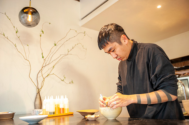 ↑食材を盛り付けるシェフの安田さん。あたたかみを感じる陶器の食器に、すべての食材がそれぞれに映えるよう、ピンセットまで駆使しながら盛り付けていく