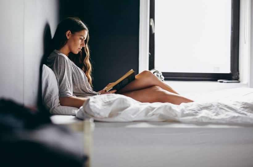 30665251 - side view shot of an attractive young woman sitting on her bed reading an interesting novel. caucasian female model in bedroom reading a book.