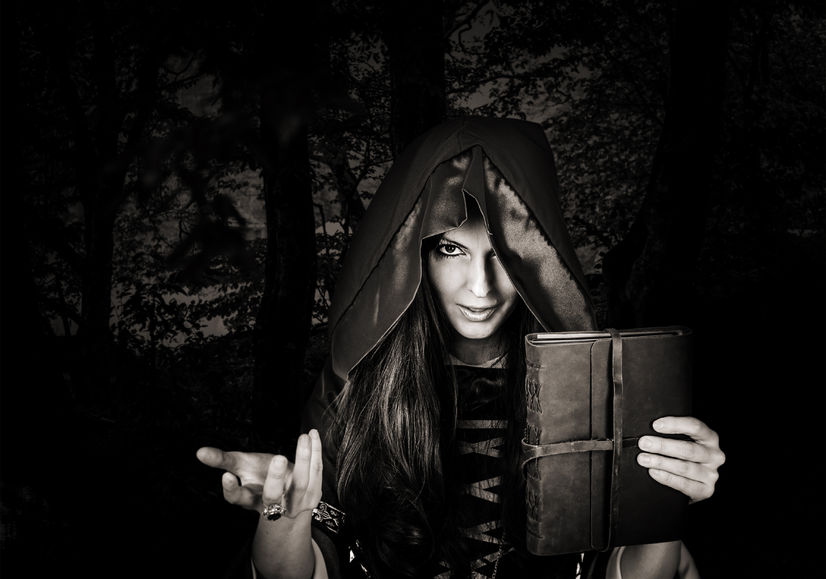 45234889 - beautiful young halloween witch wearing vintage gothic dress with hood holding magical book of spells in old leather cover in dark night forest