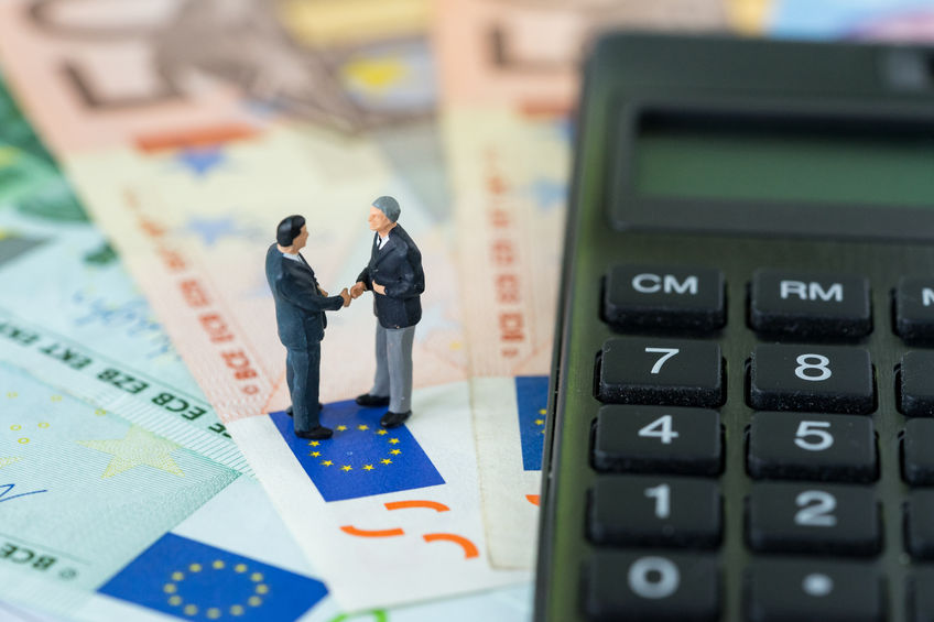 90609986 - miniature figure, businessmen shaking hand standing on pile of euro banknotes with calculator as euro economy agreement or brexit negotiation concept.
